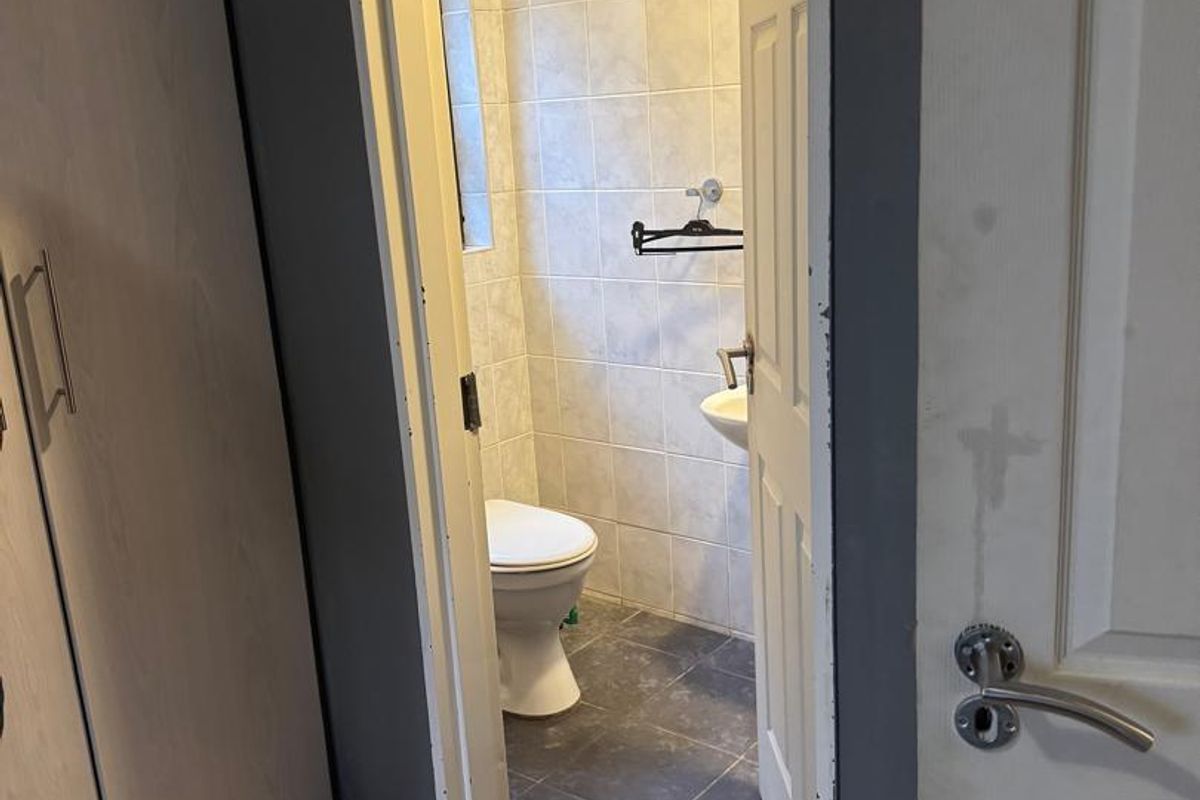 A compact bathroom featuring tiled walls and flooring, a wall-mounted basin, and a toilet, accessed via a standard interior door.