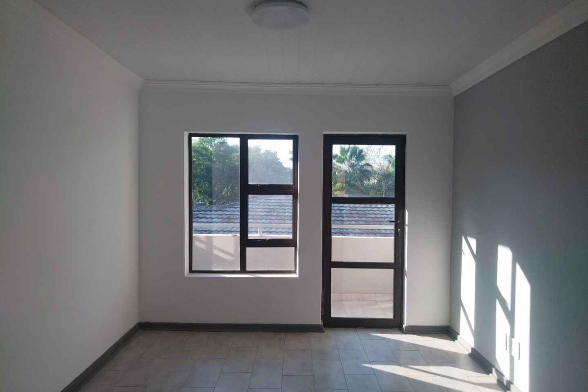 A bright, empty living room featuring tiled flooring, neutral walls, and a glass door leading to an outdoor area.