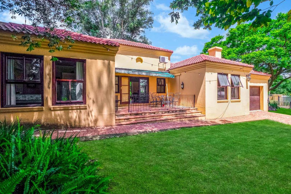 Rear view of the house featuring a brick patio, terracotta tiled roof, and well-maintained garden area with mature trees.