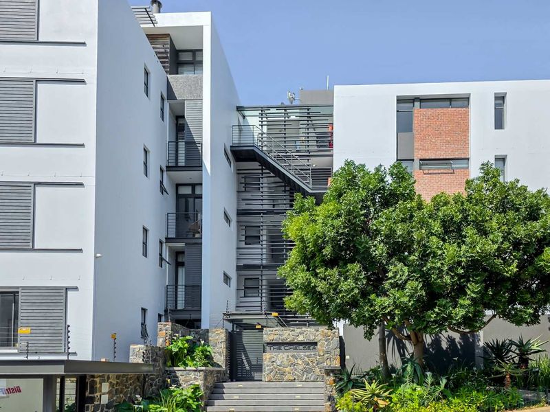 Modern apartment complex exterior featuring stone cladding, brick accents, and a central metal staircase entrance with integrated security fencing.
