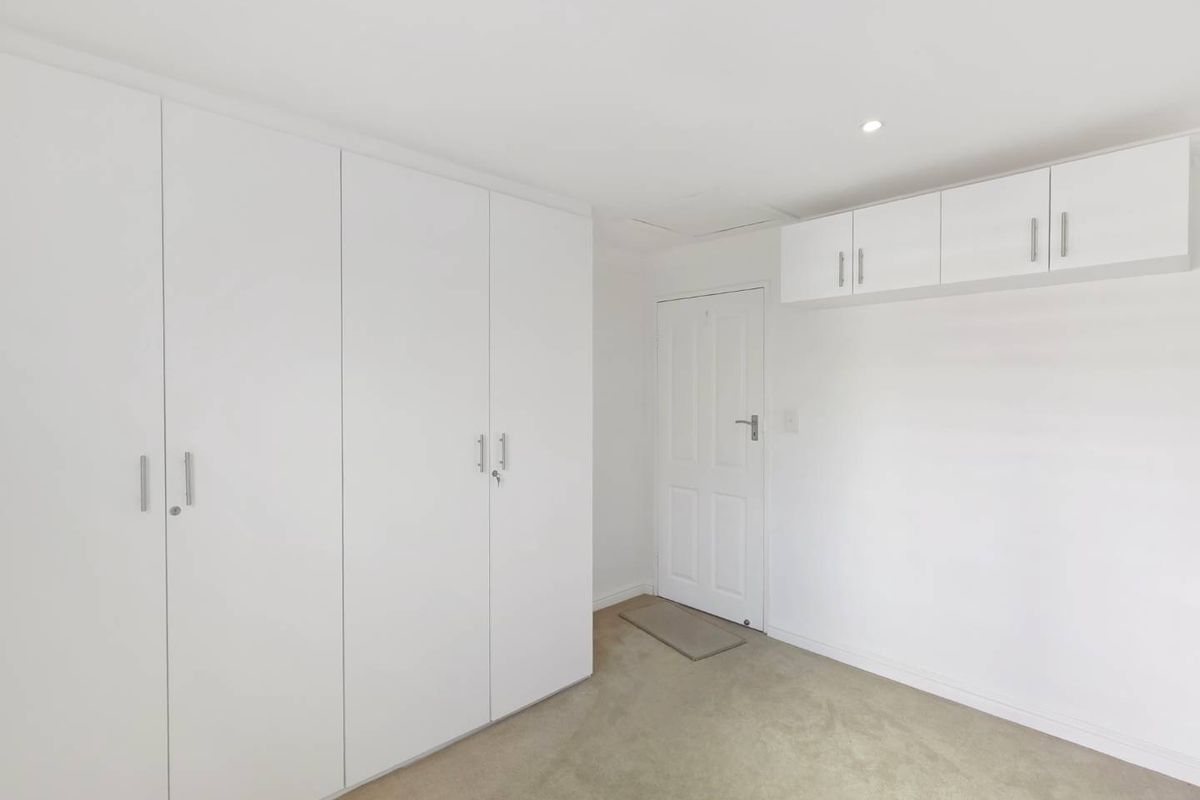 A clean, neutral bedroom featuring extensive built-in cupboard storage, overhead cabinetry, and carpeted flooring.