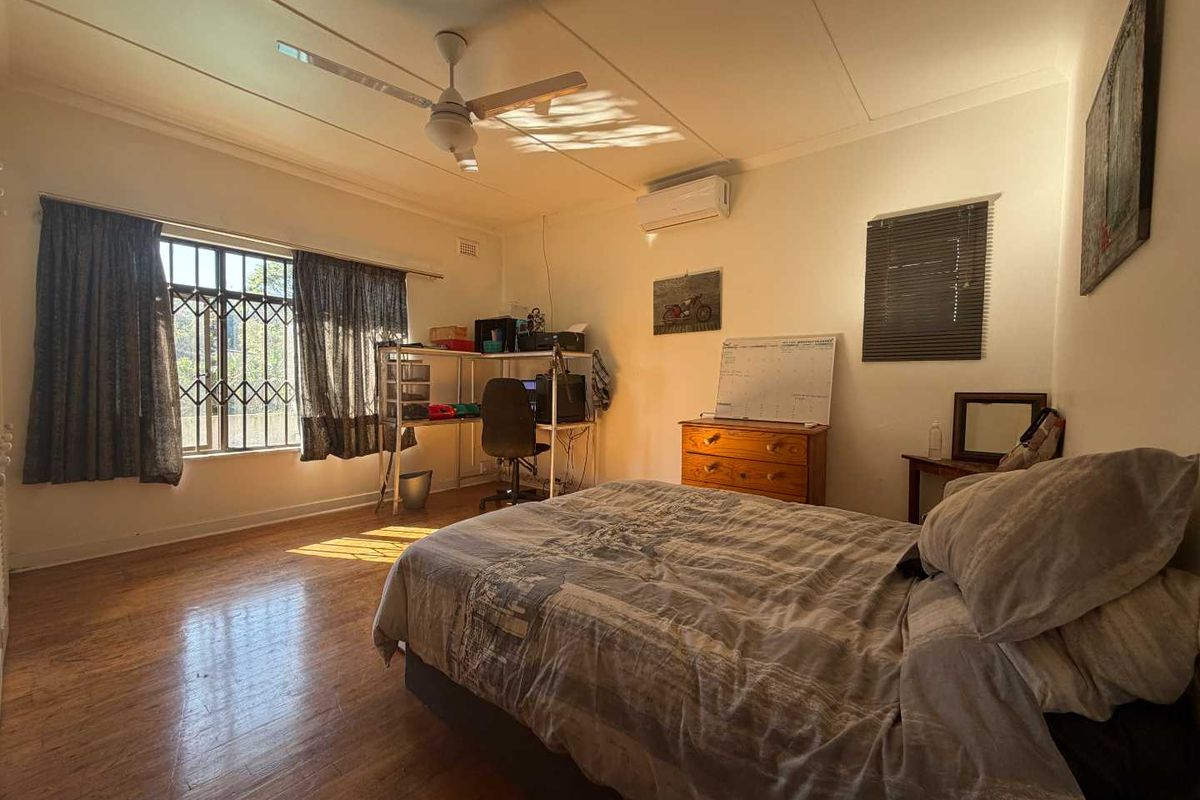 A bedroom featuring laminate flooring, a ceiling fan, and a wall-mounted split-system air conditioner, with security bars installed on the window.
