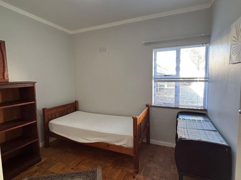 A bedroom featuring classic parquet flooring, a central ceiling light, and a window with fitted blinds.