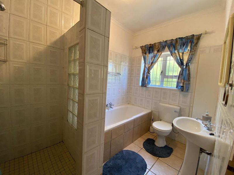 A functional bathroom featuring a separate shower with glass block detail, a bathtub, a pedestal sink, and a toilet with neutral wall tiling.