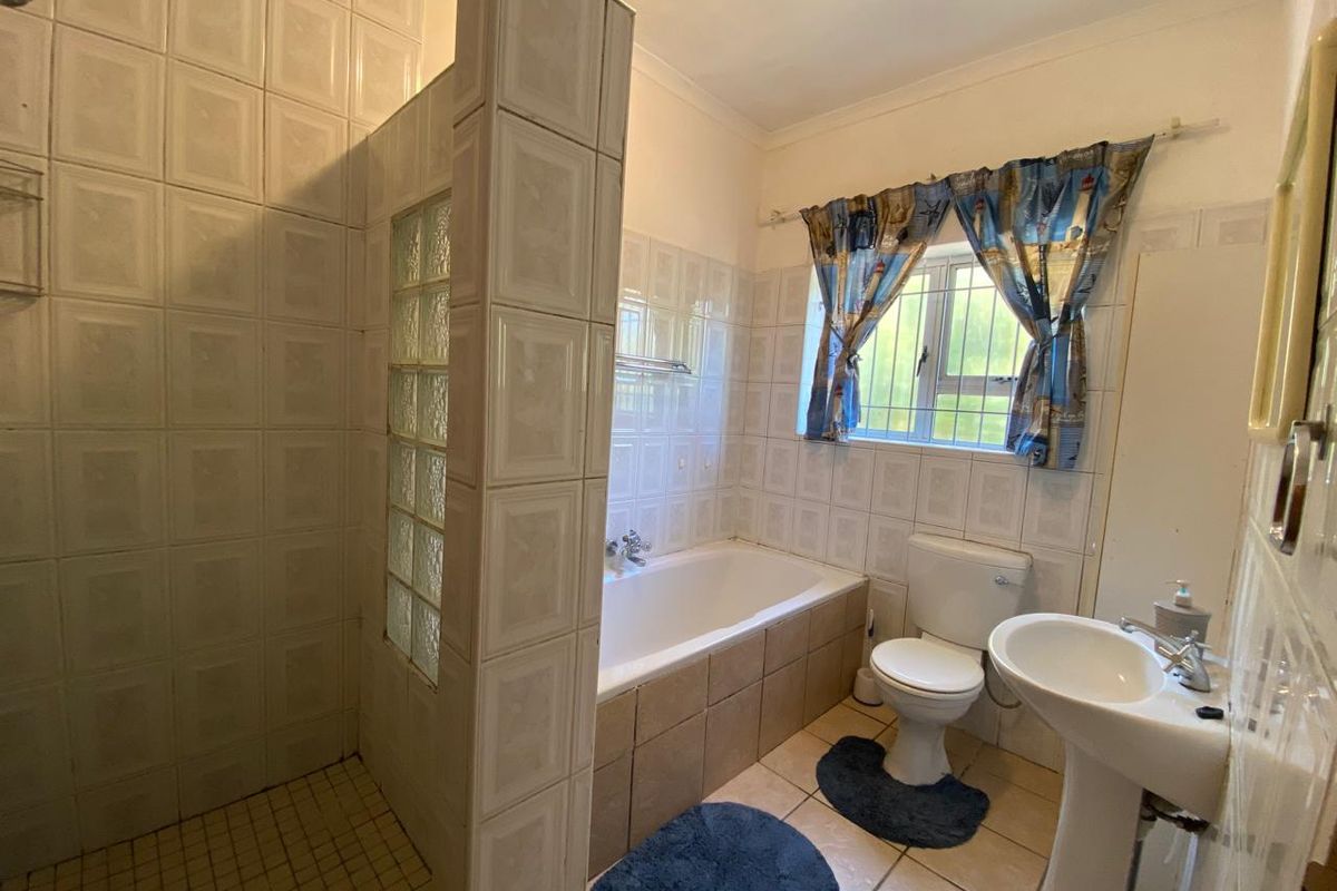 A functional bathroom featuring a separate shower with glass block detail, a bathtub, a pedestal sink, and a toilet with neutral wall tiling.