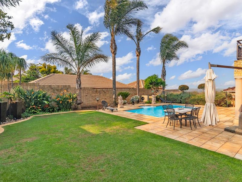 A well-maintained outdoor entertainment area featuring a swimming pool, paved patio, and established garden with a brick boundary wall.