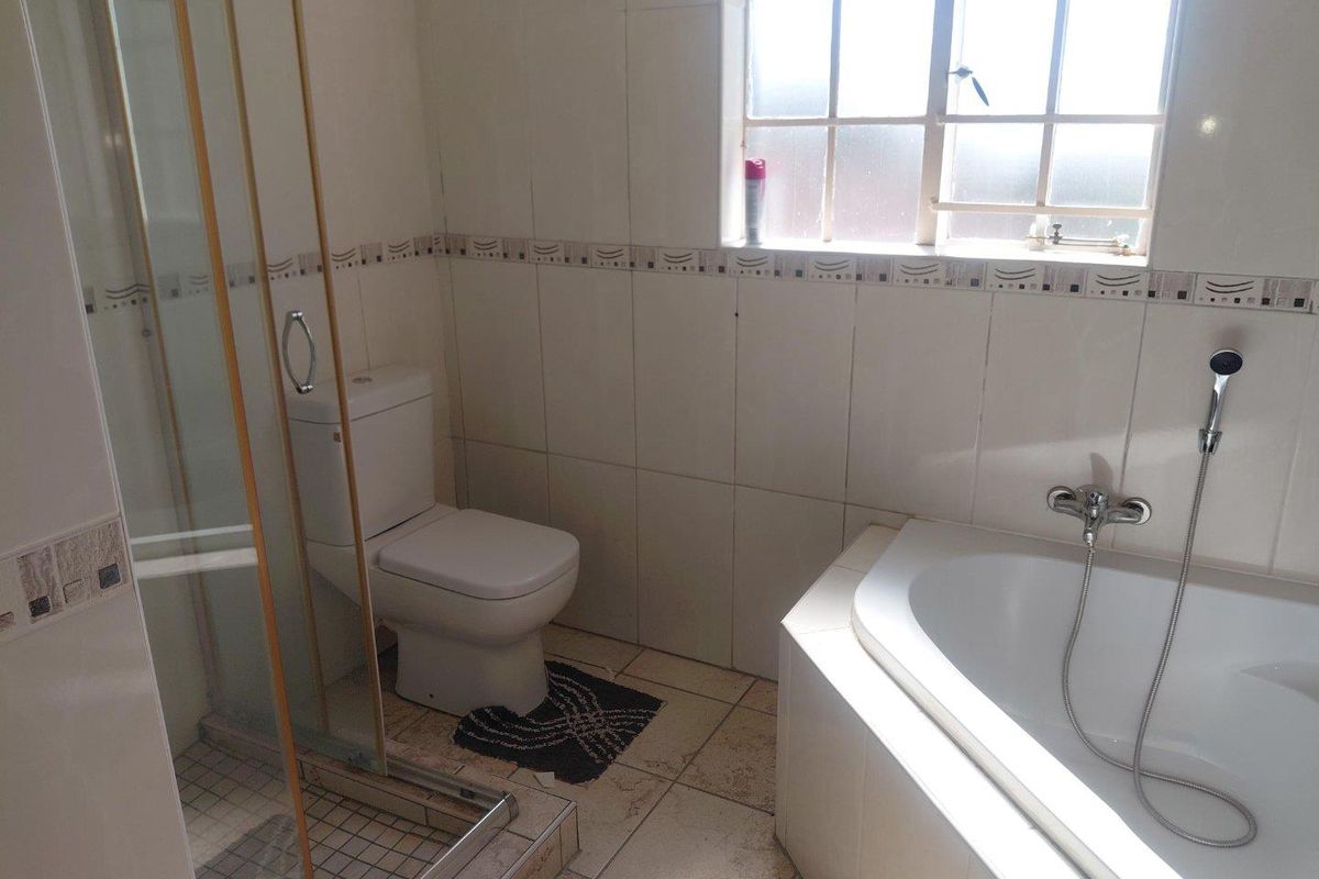 A functional bathroom featuring a shower enclosure, a bathtub with a handheld mixer, and tiled finishes throughout.