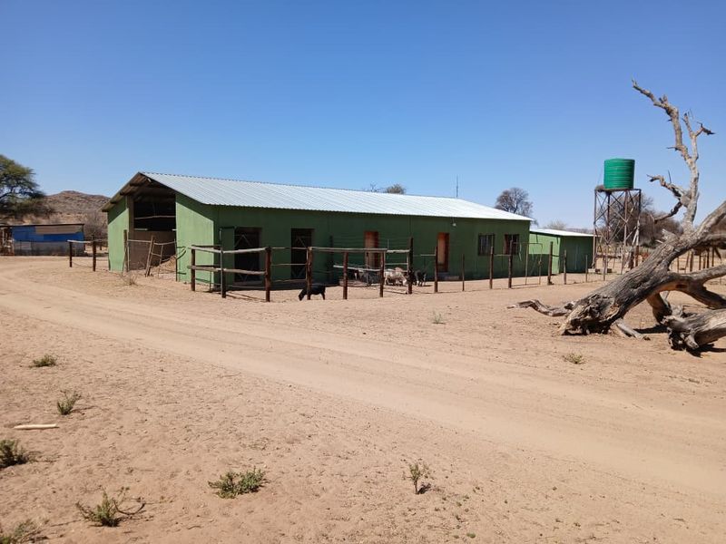 Exterior view of a rural small holding structure featuring a corrugated metal roof, timber fencing, and an elevated water storage tank.