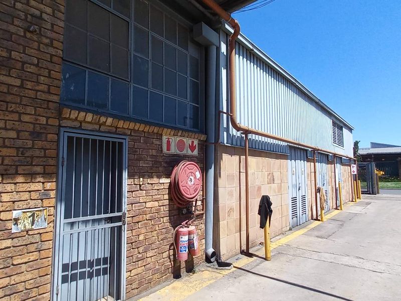 Exterior view of an industrial building featuring brick and corrugated metal cladding, equipped with fire safety infrastructure and a concrete driveway.