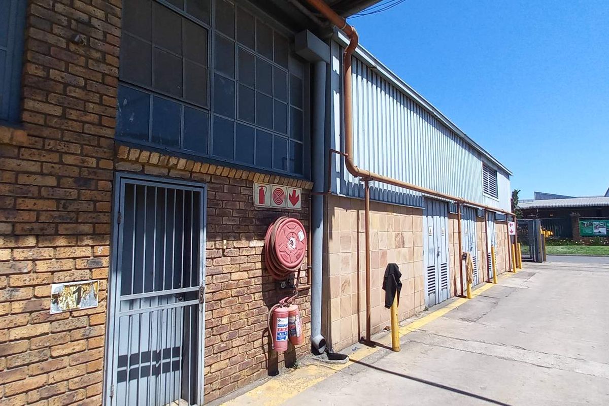Exterior view of an industrial building featuring brick and corrugated metal cladding, equipped with fire safety infrastructure and a concrete driveway.