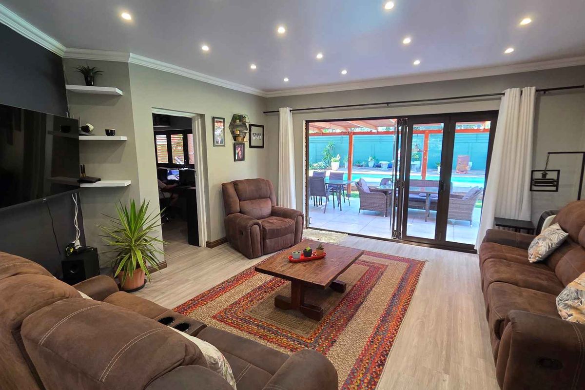 Spacious living room featuring recessed downlighting, light wood-look flooring, and large sliding glass doors providing seamless access to the outdoor patio and pool area.