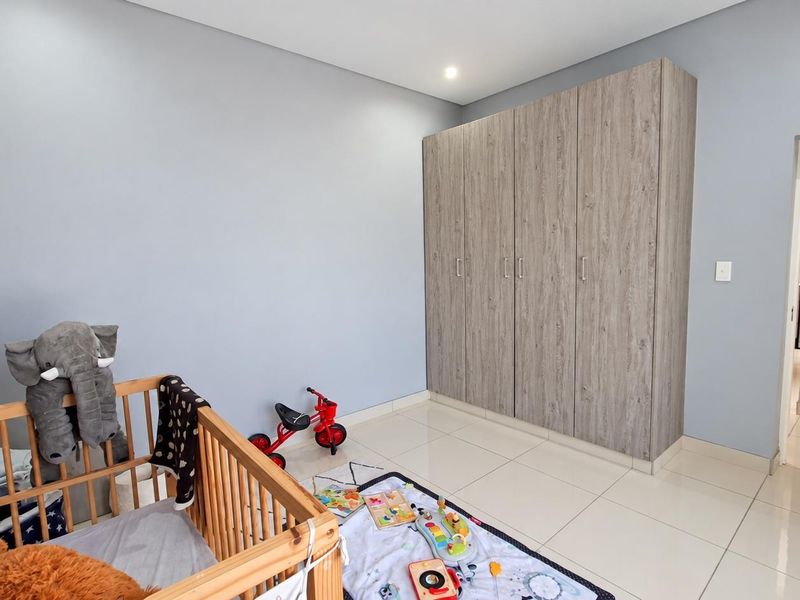 A well-maintained bedroom featuring neutral grey walls, large-format floor tiles, and modern wood-grain built-in cupboards.