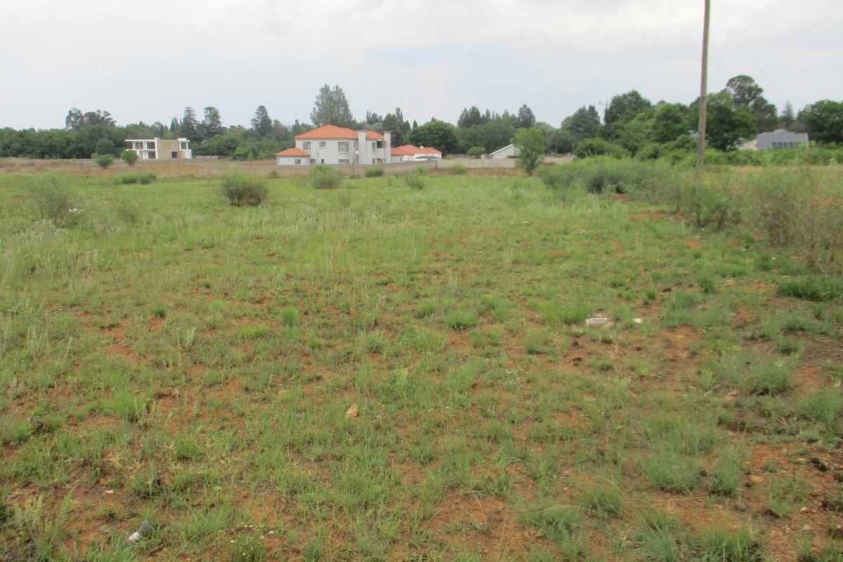 A vacant residential plot featuring natural grass cover, a boundary wall, and an adjacent utility pole in a suburban setting.