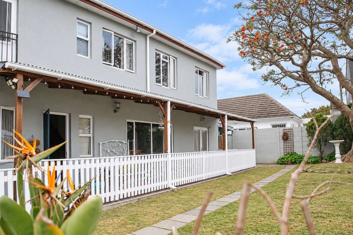 Rear view of the property featuring a covered patio with a timber pergola, white picket fencing, and a well-maintained garden area.