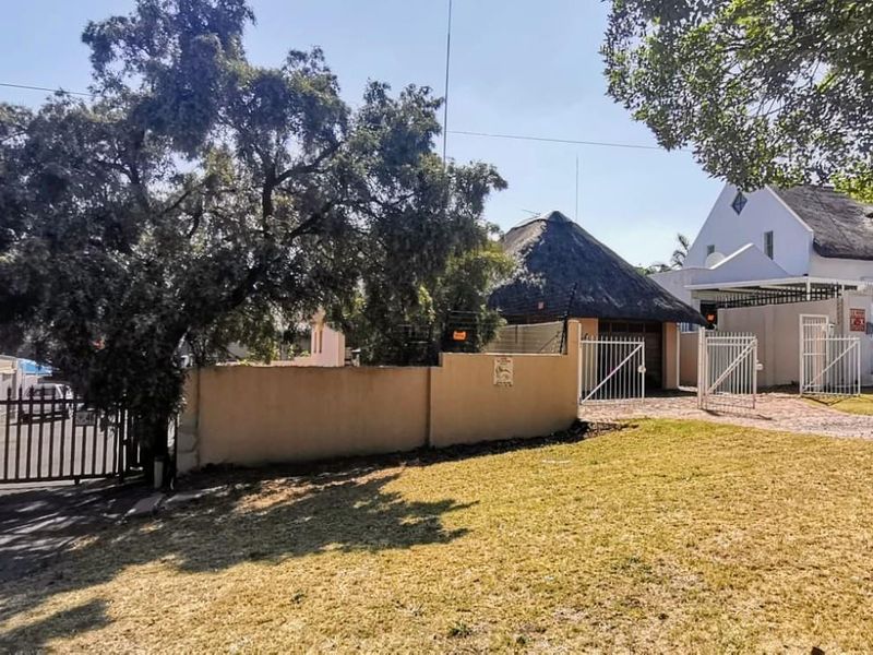 Front view of the property featuring a perimeter wall, metal security gate, paved driveway, and a structure with a traditional thatched roof.