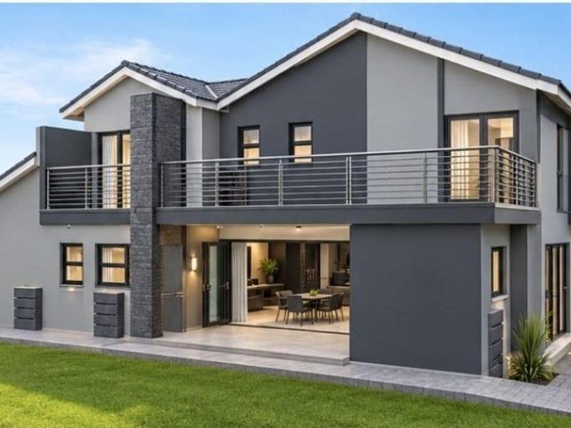 Modern double-story rear elevation featuring a spacious balcony, stone-clad chimney, and seamless indoor-outdoor flow through large sliding glass doors onto a paved patio.