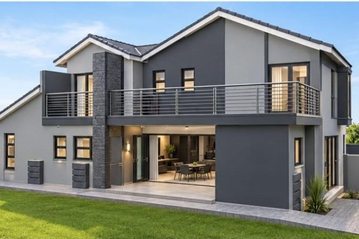 Modern double-story rear elevation featuring a spacious balcony, stone-clad chimney, and seamless indoor-outdoor flow through large sliding glass doors onto a paved patio.