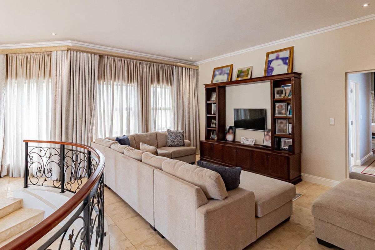 Spacious living area featuring tiled flooring, recessed lighting, and a custom built-in wooden media unit, overlooking a grand staircase with ornate wrought iron railing.