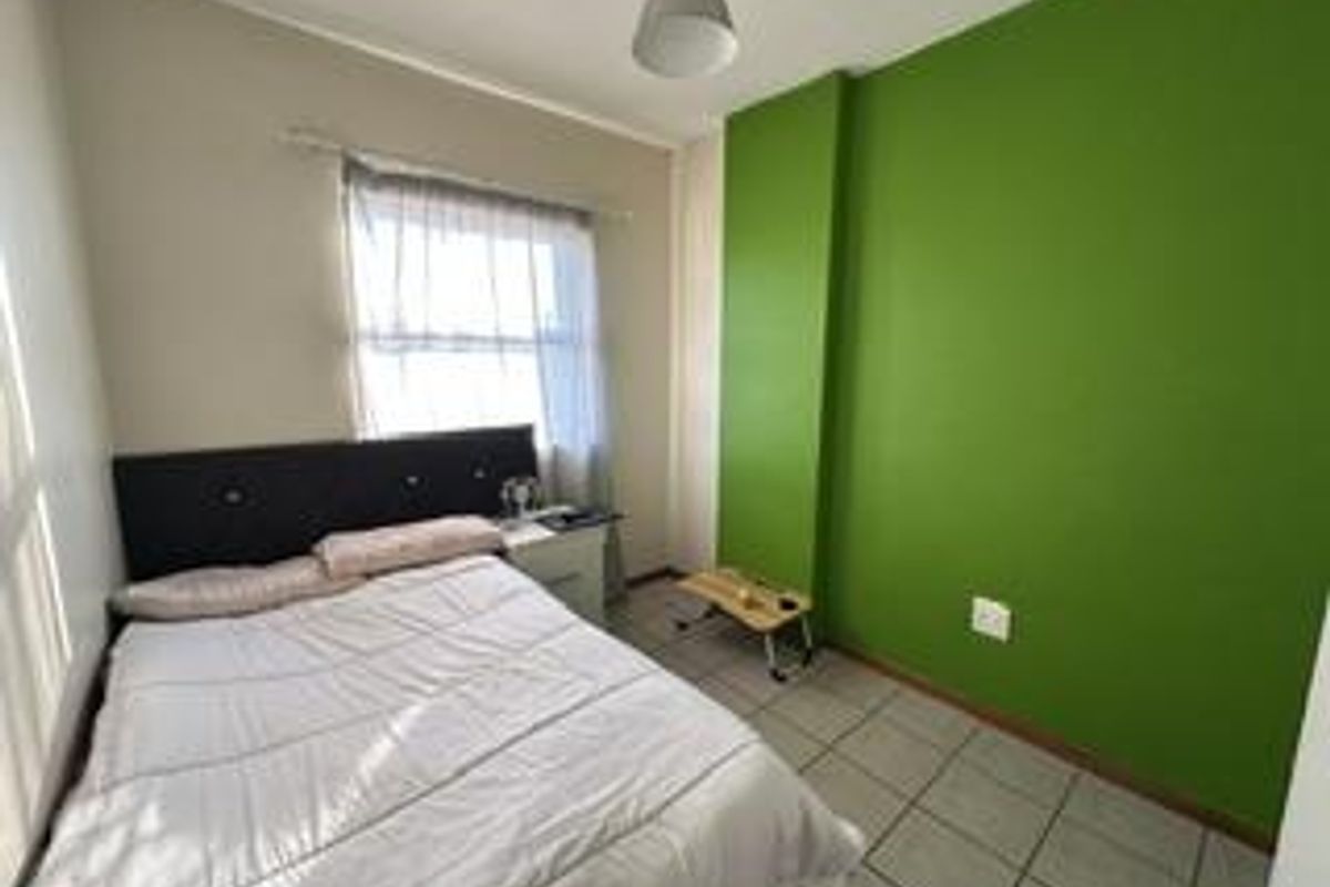 A functional bedroom featuring tiled flooring and a large window with a curtain rail, providing a simple and practical living space.