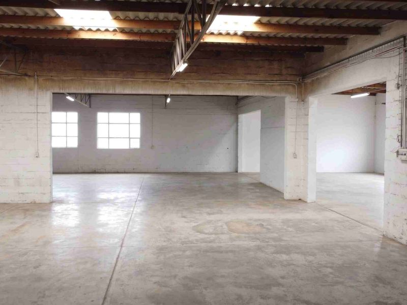 Spacious industrial utility area featuring exposed timber roof trusses, skylights, concrete flooring, and exposed brick walls, suitable for various commercial or storage applications.