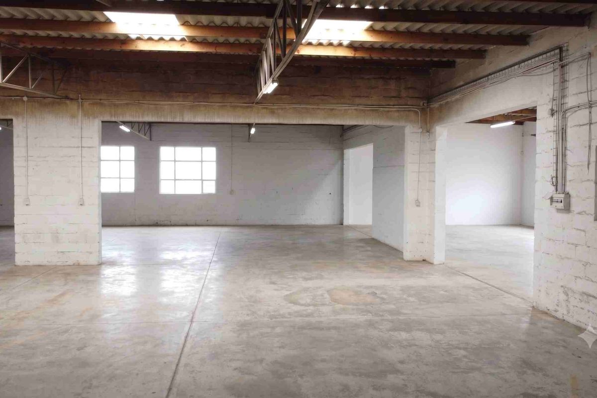 Spacious industrial utility area featuring exposed timber roof trusses, skylights, concrete flooring, and exposed brick walls, suitable for various commercial or storage applications.