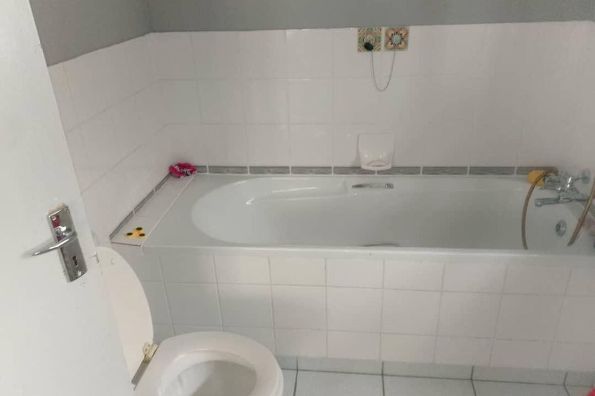 A functional bathroom featuring a built-in bathtub with tiled surround and a standard toilet.