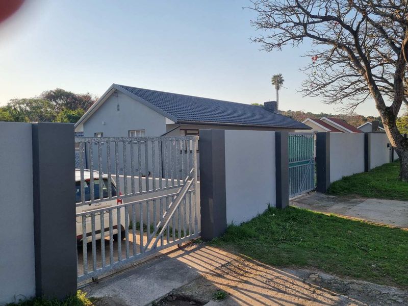 Front view of the property featuring a secure perimeter wall, metal driveway gate, and a well-maintained tiled roof structure.