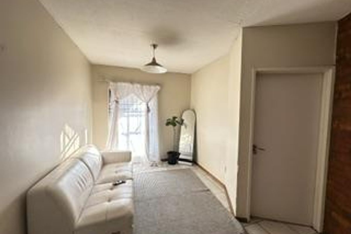 A simple living room area featuring tiled flooring and a central pendant light fixture, providing a functional and neutral space.