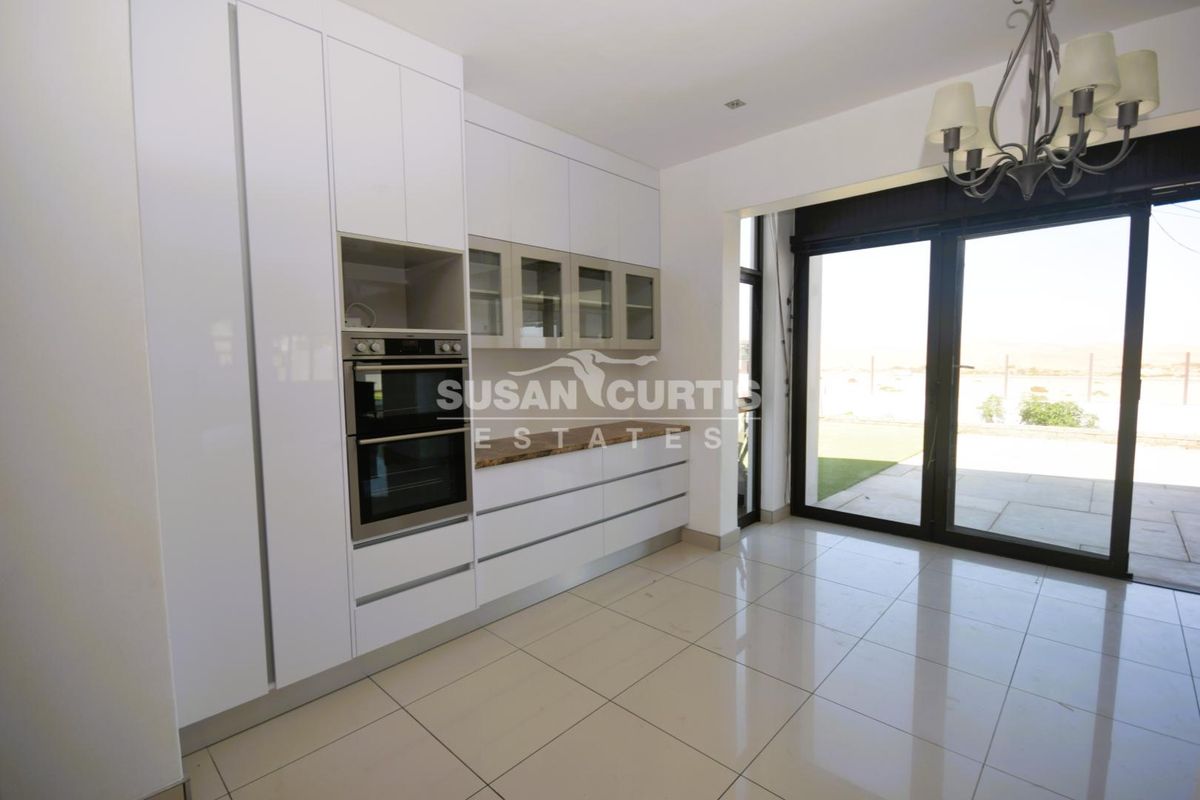Modern kitchen featuring high-gloss white cabinetry, built-in double oven, and tiled flooring with direct access to the outdoor patio area.