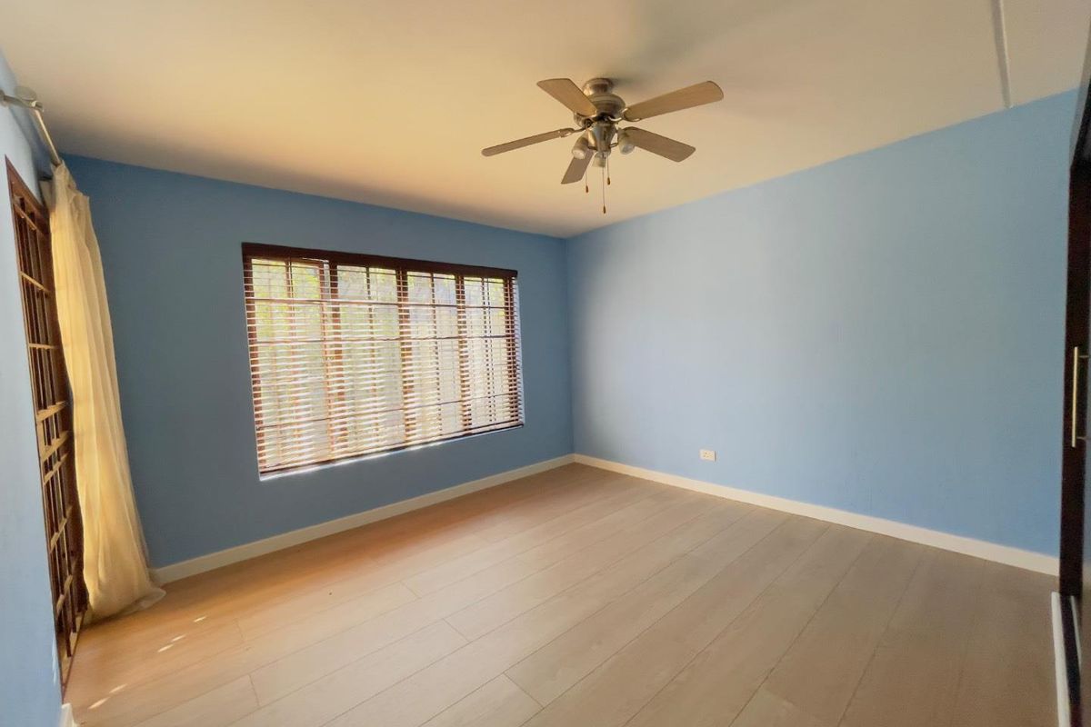 A bright, empty bedroom featuring light-toned laminate flooring, a ceiling fan, and window blinds, offering a clean and neutral space ready for personalization.