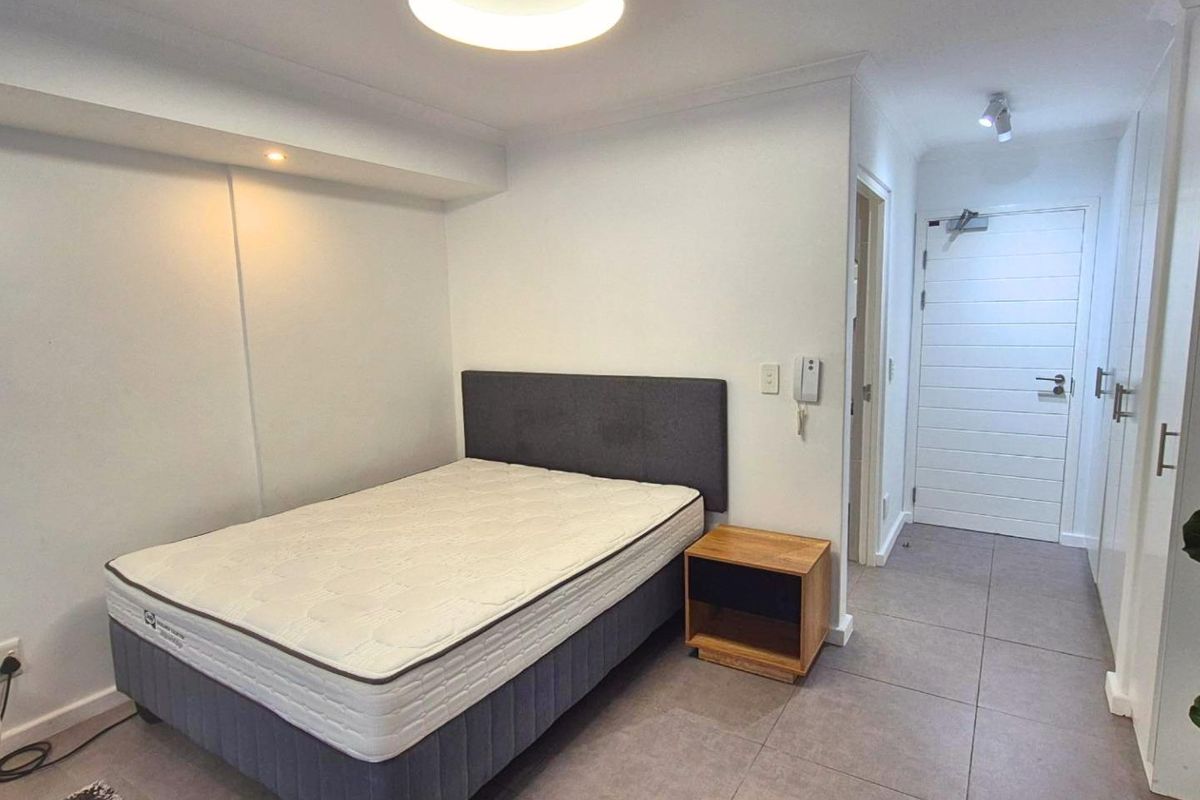 A clean bedroom featuring tiled flooring, built-in wardrobe storage, and modern recessed lighting, providing a functional and neutral living space.