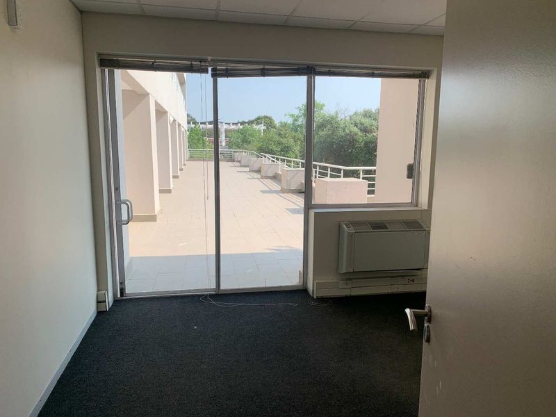 An empty office space featuring carpeted flooring, a wall-mounted air conditioning unit, and large sliding glass doors leading to an outdoor balcony.