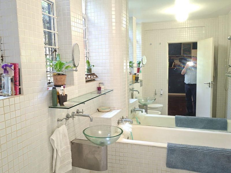 A tiled bathroom featuring a glass vessel sink, wall-mounted faucet, built-in bathtub with shower, and a large mirror.