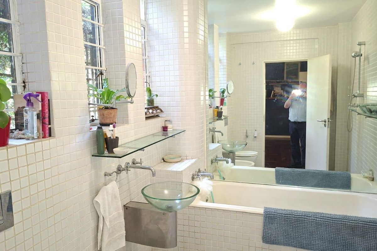 A tiled bathroom featuring a glass vessel sink, wall-mounted faucet, built-in bathtub with shower, and a large mirror.