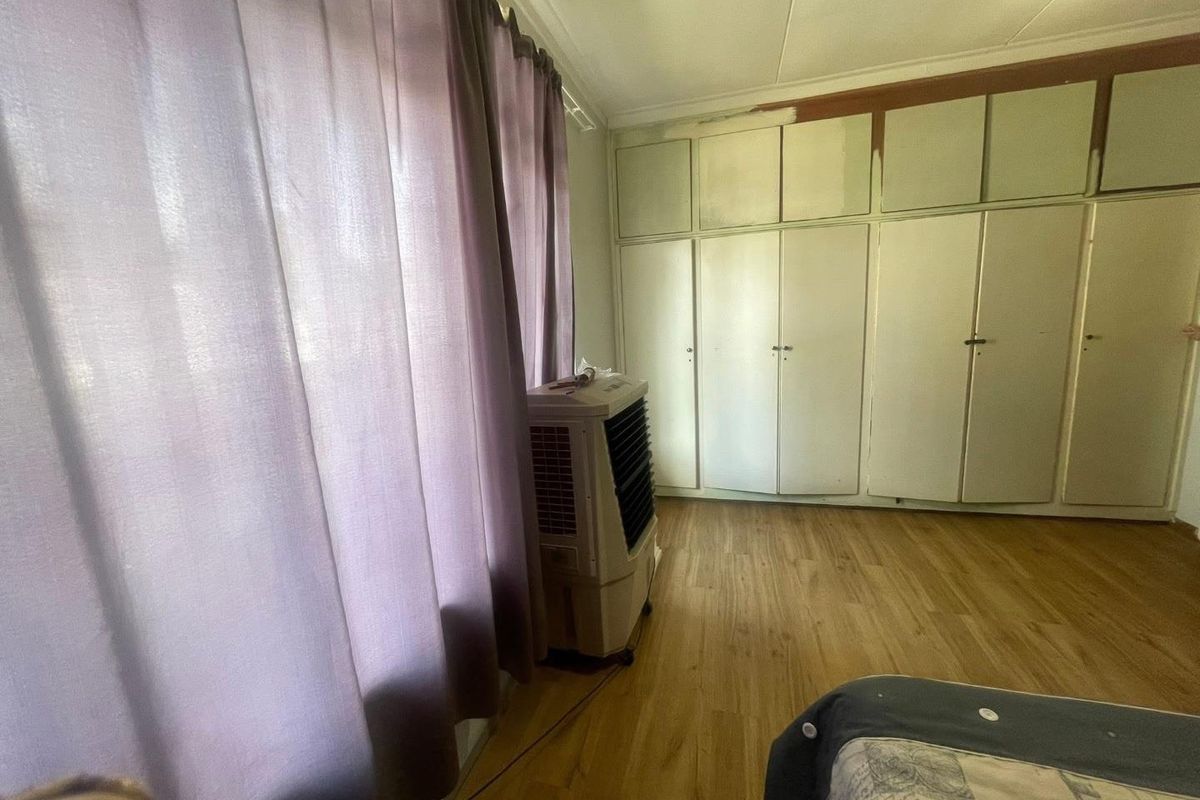 A bedroom featuring built-in storage cupboards and wood-look flooring, currently requiring minor cosmetic finishing and updates to the wall paint.
