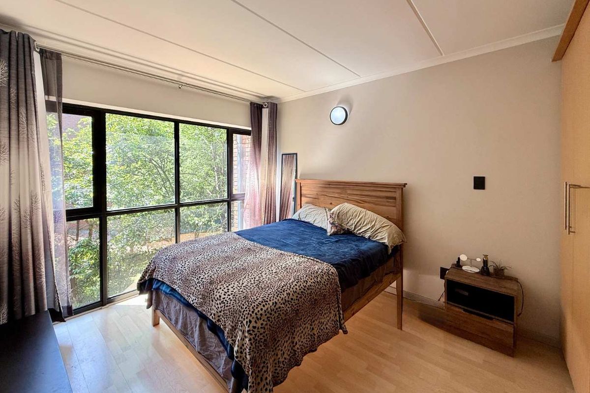 A bedroom featuring large floor-to-ceiling windows with natural light, light wood-look flooring, and built-in wardrobe storage.