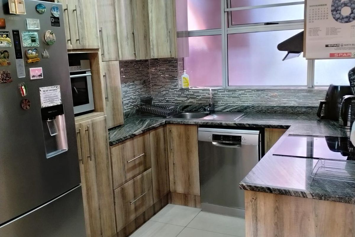 Compact kitchen featuring wood-look cabinetry, granite countertops, mosaic tile backsplash, integrated oven, and stainless steel dishwasher.