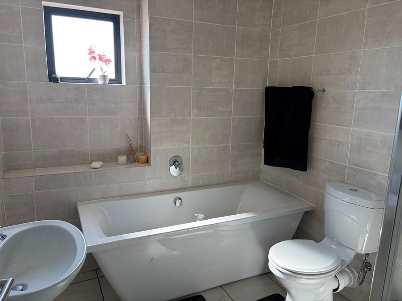 A modern bathroom featuring a freestanding bathtub, pedestal basin, toilet, and neutral wall tiling with a convenient built-in recessed shelf.