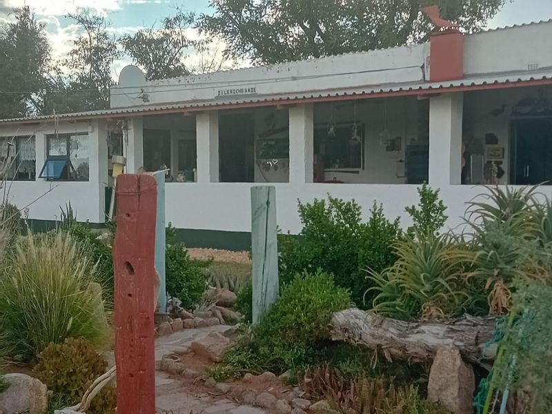 A rustic lodge exterior featuring a covered patio, concrete pillars, and a well-established garden with a stone pathway leading to the entrance.