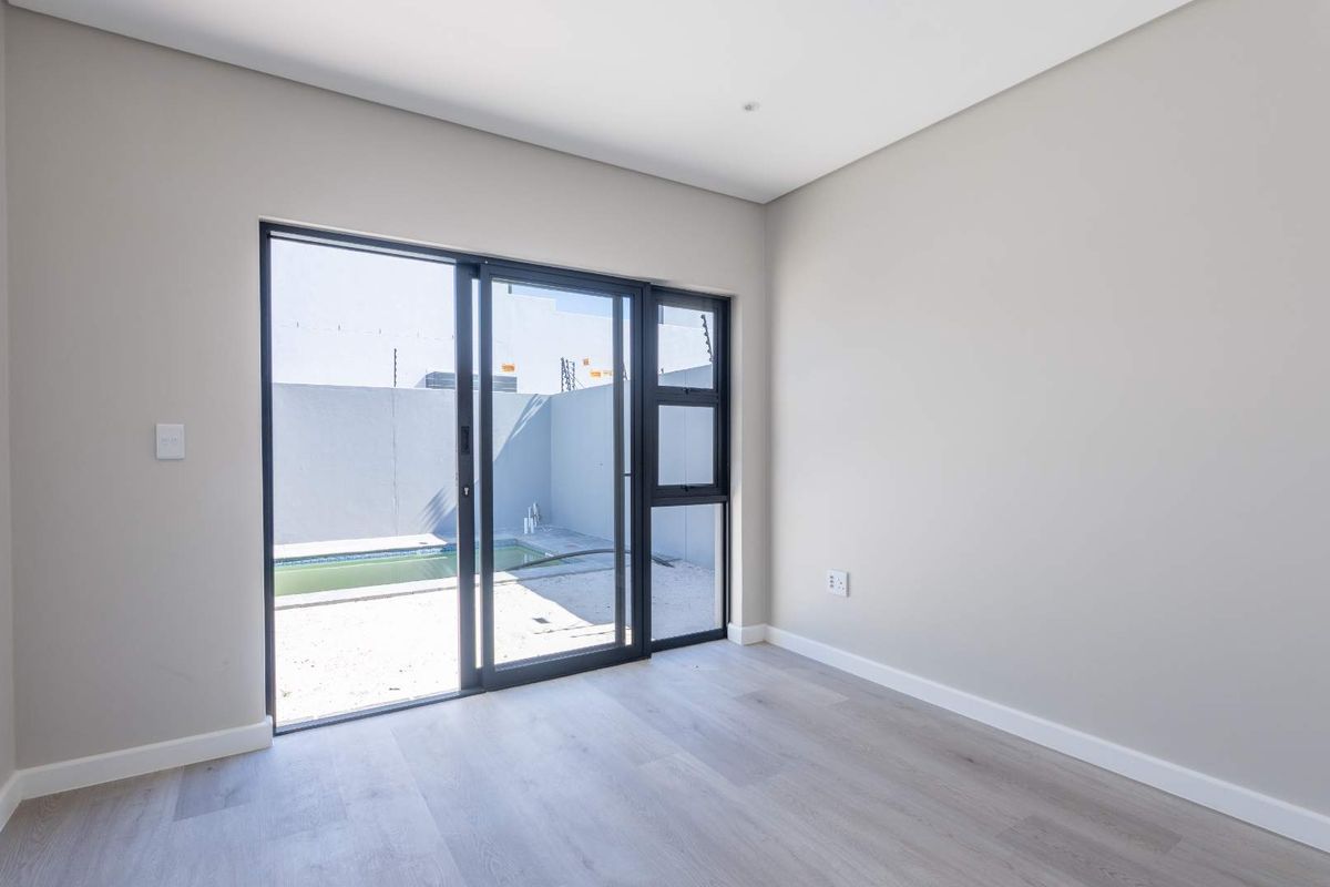 A bright, empty bedroom featuring modern laminate flooring and a large sliding glass door providing direct access to the outdoor pool area.