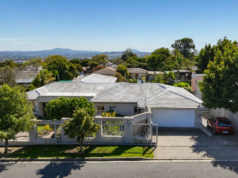 Aerial view of a residential property featuring a tiled roof, paved driveway, secure perimeter wall with gate, and a garage.