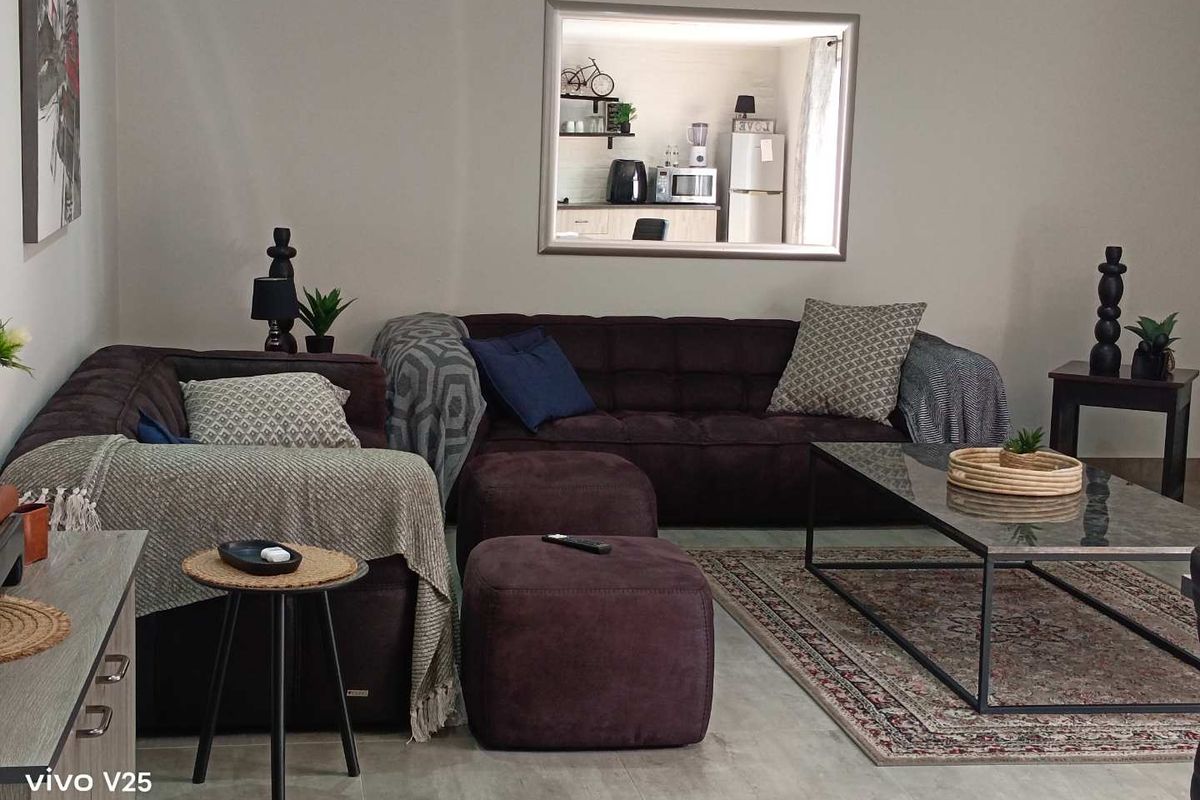 A comfortable living room featuring neutral tiled flooring and a large interior window providing a view into the adjacent kitchen area.