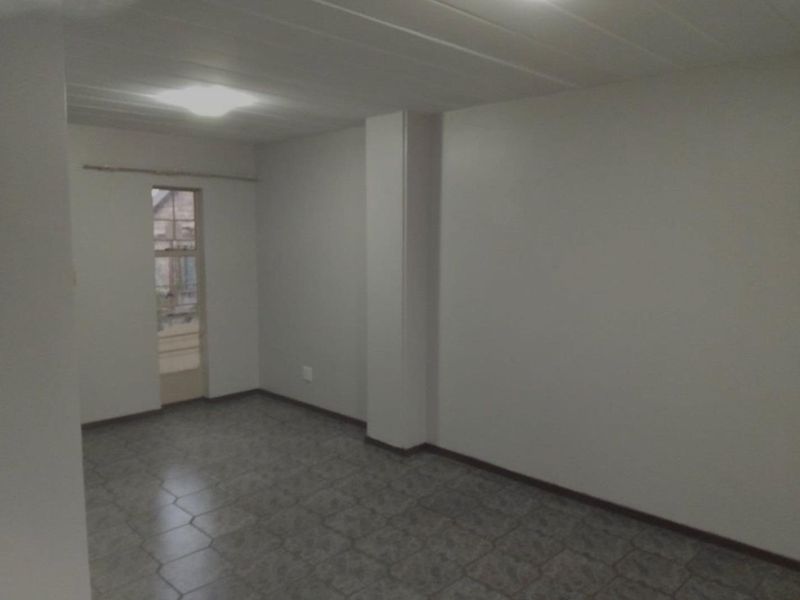 An empty, neutral-toned living area featuring tiled flooring and a simple ceiling light fixture, providing a blank canvas for interior design.