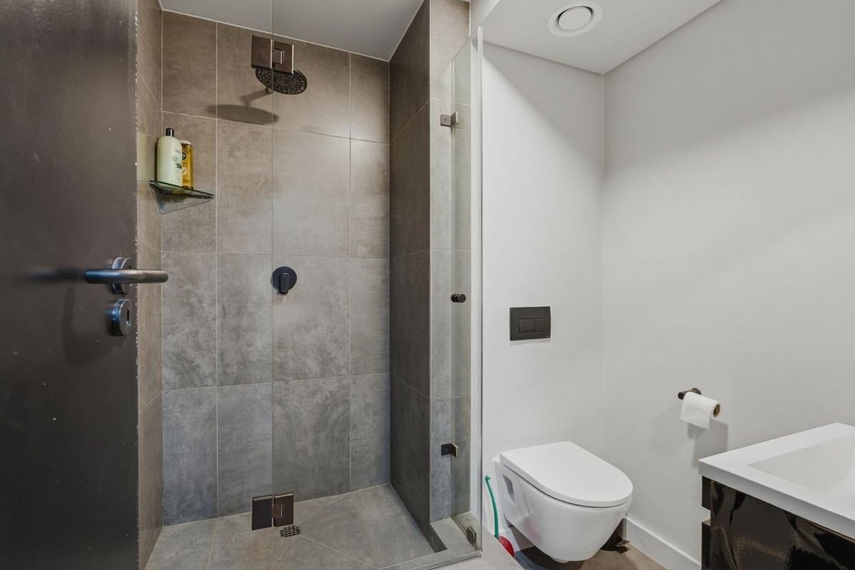 Modern bathroom featuring a walk-in shower with a rain shower head, glass screen, wall-mounted toilet, and a vanity basin.