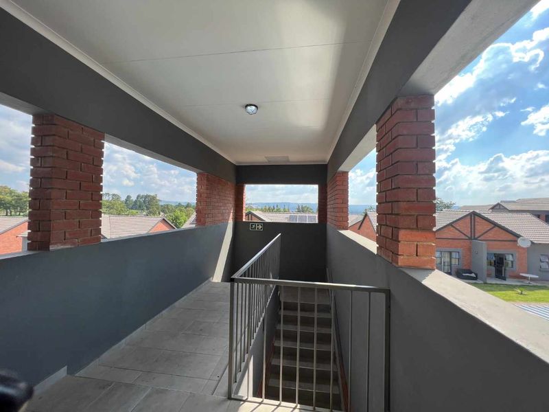 An open-air apartment hallway featuring exposed brick pillars, metal balustrades, and tiled flooring, providing access to the staircase.