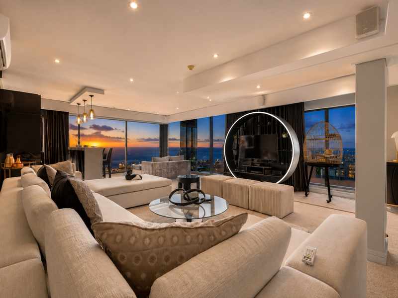 Spacious open-plan living area featuring floor-to-ceiling windows with panoramic sunset views, recessed lighting, and modern architectural bulkheads in a high-end penthouse setting.