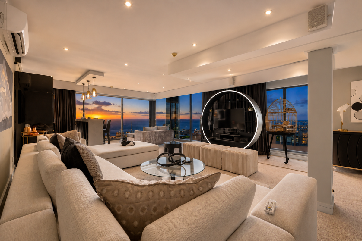 Spacious open-plan living area featuring floor-to-ceiling windows with panoramic sunset views, recessed lighting, and modern architectural bulkheads in a high-end penthouse setting.