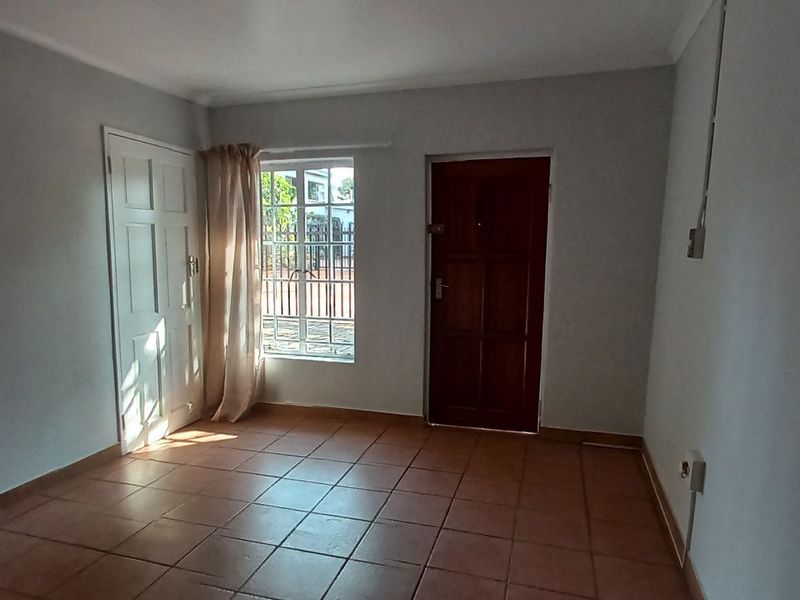 An empty living area featuring tiled flooring, a timber entrance door, and a window fitted with security burglar bars.