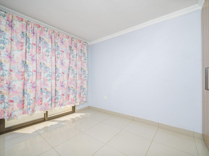 A bright, empty bedroom featuring neutral tiled flooring, crown molding, and a built-in wardrobe with sliding glass doors leading to an outdoor area.