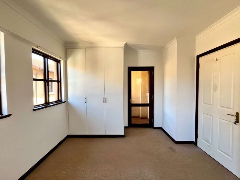 A vacant bedroom featuring built-in cupboards, carpeted flooring, and a glass-panelled door leading to an adjacent space.